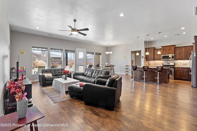 living room featuring dark wood-style floors, recessed lighting, baseboards, and ceiling fan with notable chandelier