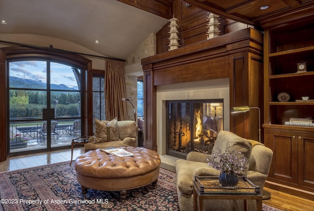 living area featuring a premium fireplace, built in features, a mountain view, vaulted ceiling, and light wood-type flooring