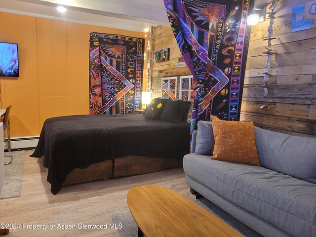 bedroom with baseboard heating, wooden walls, and wood-type flooring