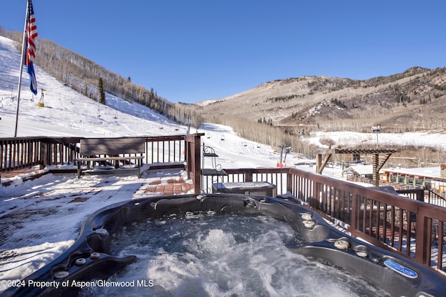 snow covered deck with a mountain view and a hot tub