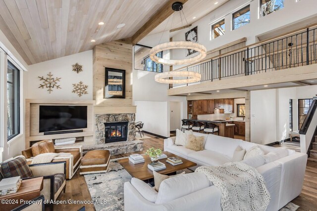 living room featuring wood ceiling, wood-type flooring, high vaulted ceiling, beamed ceiling, and a stone fireplace