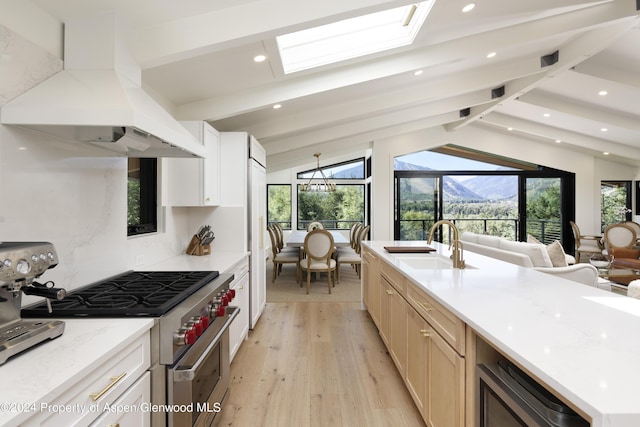 kitchen featuring ventilation hood, light wood-style flooring, a sink, open floor plan, and stainless steel range