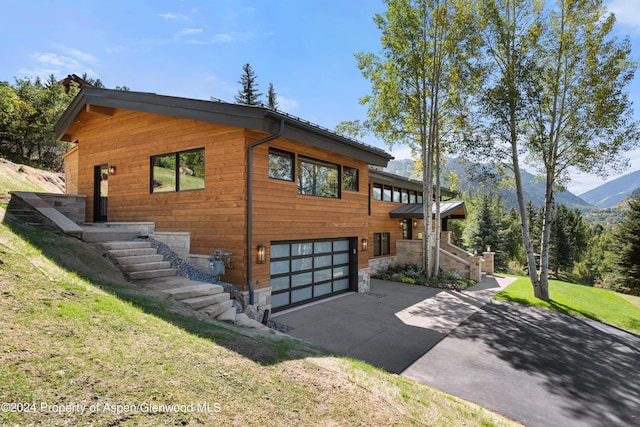 view of front facade featuring concrete driveway, stone siding, an attached garage, a mountain view, and a front yard
