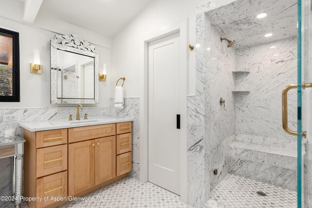 full bath featuring tile walls, a wainscoted wall, vanity, and a marble finish shower