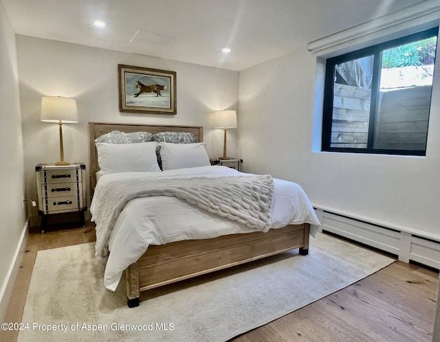 bedroom with a baseboard heating unit, wood finished floors, and recessed lighting