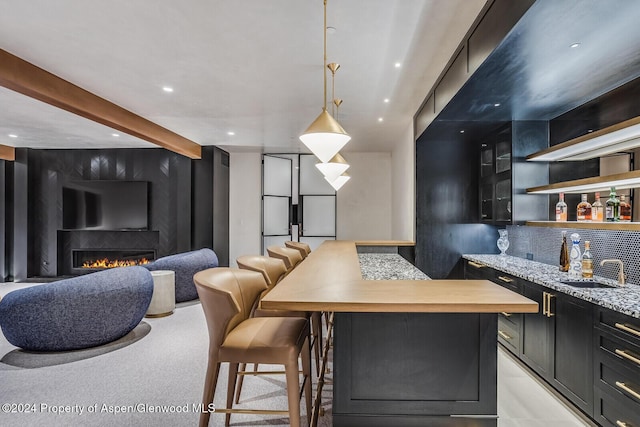 kitchen with light stone countertops, tasteful backsplash, a breakfast bar, a large fireplace, and decorative light fixtures