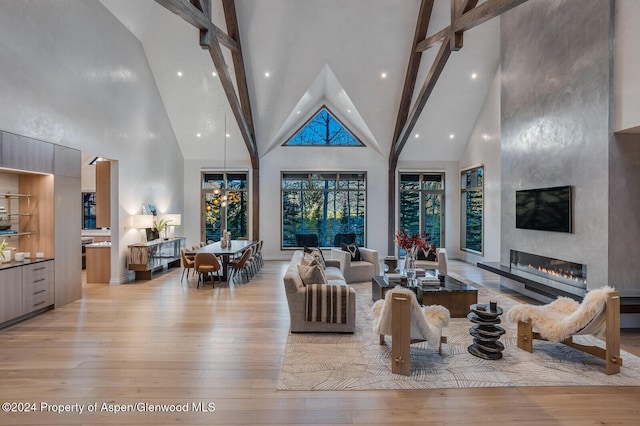 living room featuring a large fireplace, light hardwood / wood-style floors, beam ceiling, and a high ceiling