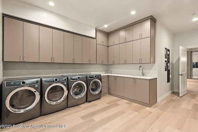 clothes washing area with washing machine and dryer, sink, cabinets, and light wood-type flooring