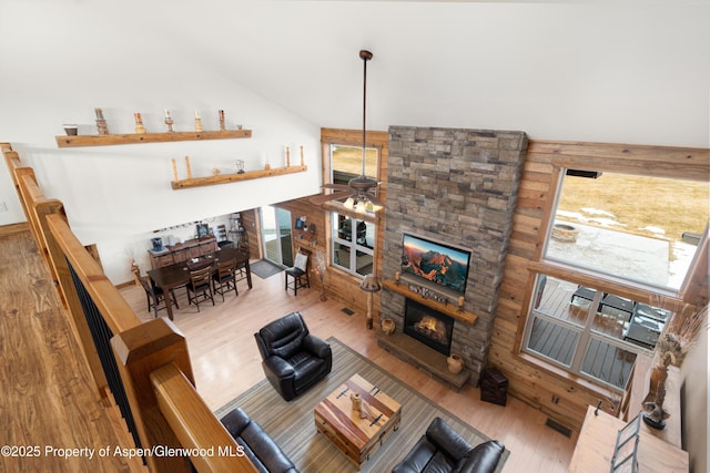 living room with ceiling fan, high vaulted ceiling, a stone fireplace, and hardwood / wood-style floors