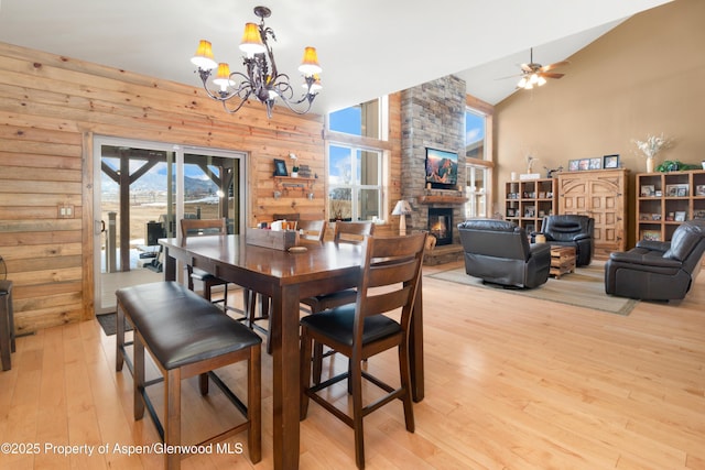 dining room featuring ceiling fan with notable chandelier, a fireplace, wood walls, lofted ceiling, and light hardwood / wood-style floors