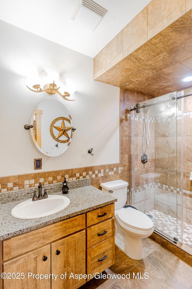 bathroom featuring walk in shower, vanity, toilet, and tile walls