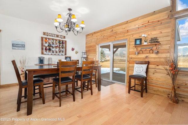 dining space with light hardwood / wood-style floors, a chandelier, and wood walls