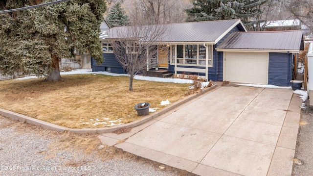 ranch-style home with a garage, concrete driveway, metal roof, and a front lawn