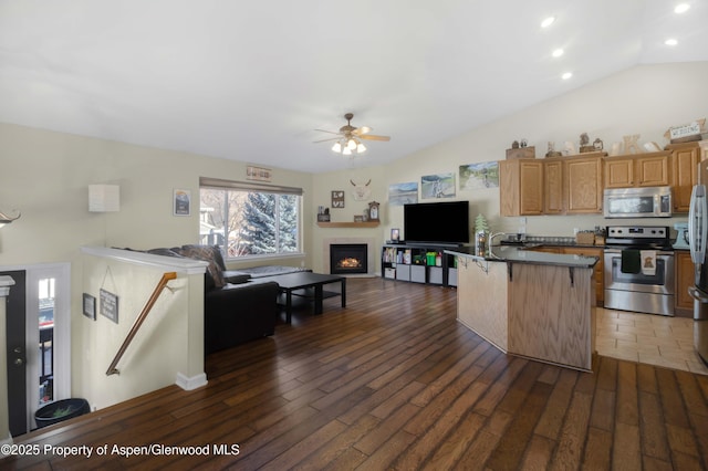 kitchen with a breakfast bar area, ceiling fan, stainless steel appliances, dark hardwood / wood-style flooring, and vaulted ceiling