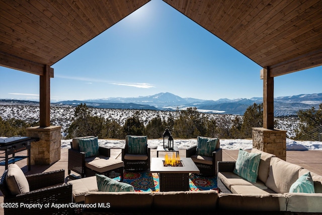 snow covered patio with a mountain view and an outdoor living space with a fire pit