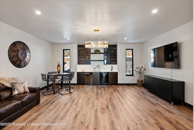 living room with an inviting chandelier, bar, and light wood-type flooring