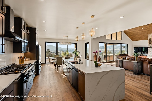 kitchen featuring pendant lighting, a spacious island, sink, range with two ovens, and wall chimney exhaust hood