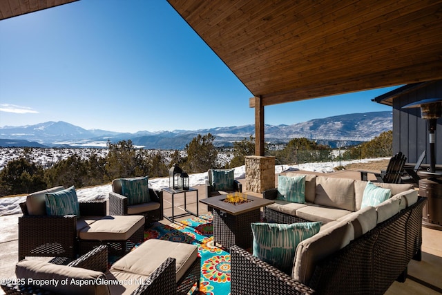 snow covered patio featuring a mountain view and an outdoor living space with a fire pit