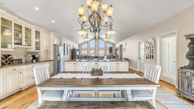 dining space featuring an inviting chandelier, vaulted ceiling, and light hardwood / wood-style flooring