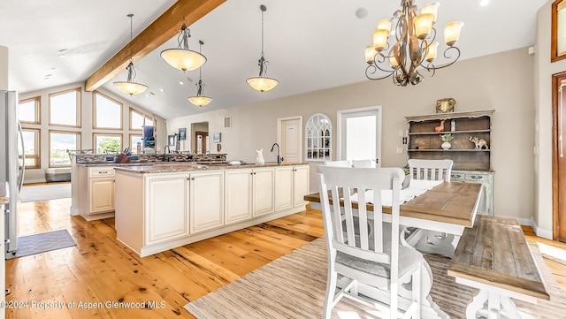 kitchen with a kitchen island with sink, an inviting chandelier, beamed ceiling, decorative light fixtures, and light hardwood / wood-style floors