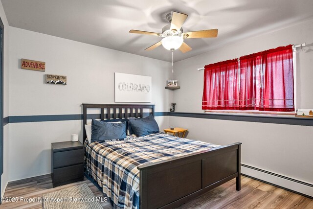 bedroom featuring wood finished floors, a ceiling fan, and a baseboard radiator