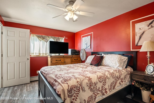 bedroom featuring a baseboard heating unit, wood finished floors, and ceiling fan