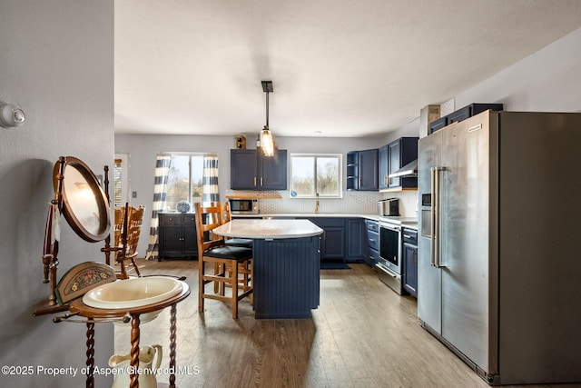 kitchen with backsplash, wall chimney range hood, light wood-type flooring, light countertops, and stainless steel appliances