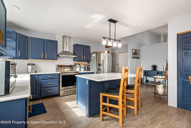 kitchen featuring light countertops, blue cabinetry, wall chimney exhaust hood, and appliances with stainless steel finishes