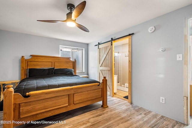 bedroom with ensuite bath, a barn door, a ceiling fan, and light wood-type flooring