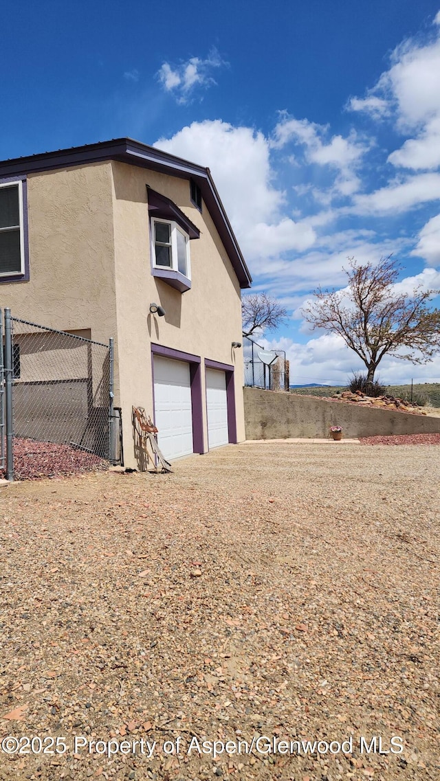 3294 County Road 103, Craig, CO 81625 - back of house with a garage, dirt driveway, stucco siding, and fence