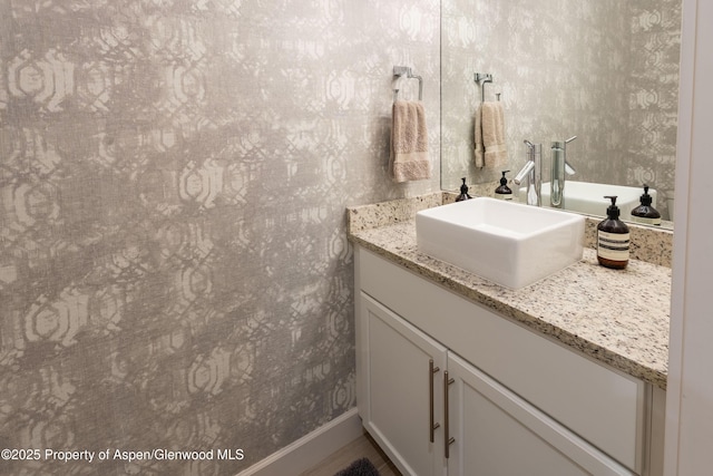 bathroom featuring vanity, baseboards, and wallpapered walls