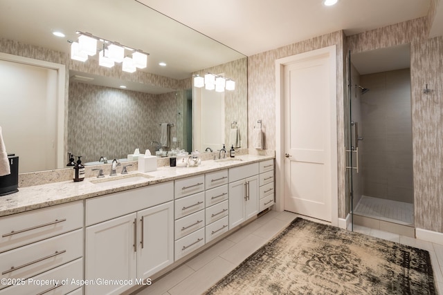 bathroom with wallpapered walls, a shower stall, double vanity, and a sink