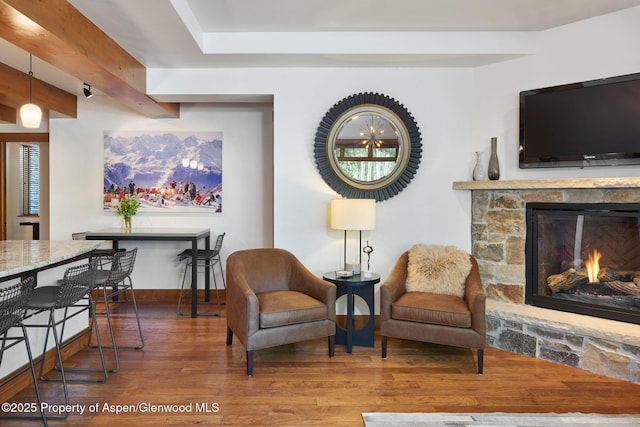 sitting room featuring wood-type flooring, a stone fireplace, and beam ceiling