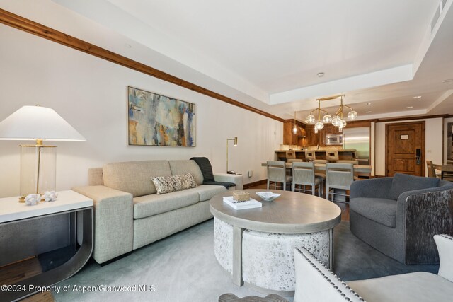 carpeted living room featuring a chandelier and a raised ceiling