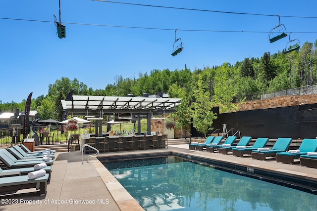 view of swimming pool with exterior bar, a pergola, and a patio area