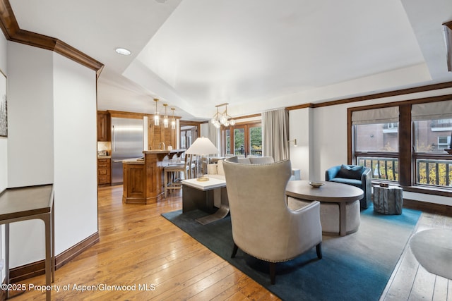 living room featuring light wood-style flooring, a notable chandelier, baseboards, a raised ceiling, and crown molding