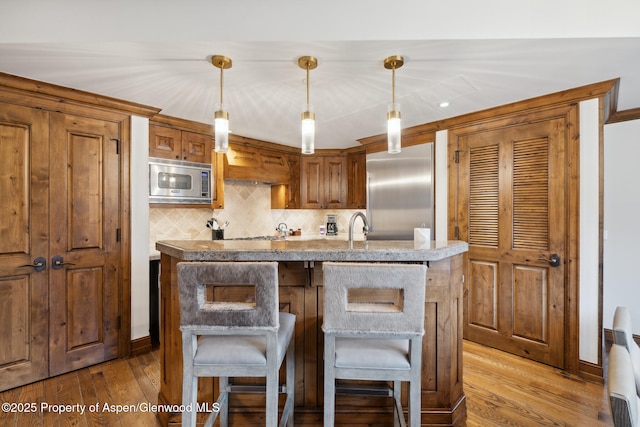 kitchen with tasteful backsplash, wood finished floors, an island with sink, and built in appliances