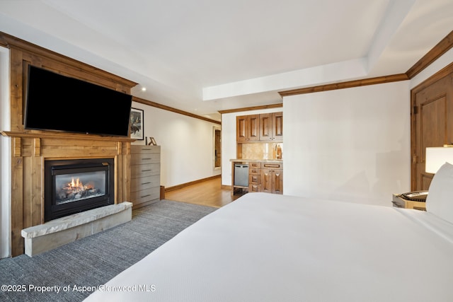 bedroom featuring baseboards, wood finished floors, crown molding, and a glass covered fireplace