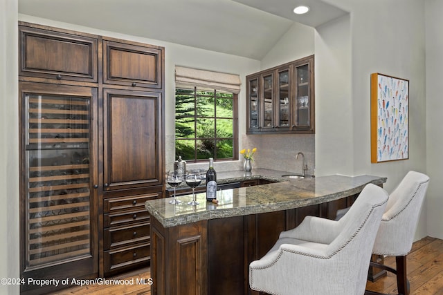 bar featuring dark brown cabinetry, stone counters, sink, and vaulted ceiling