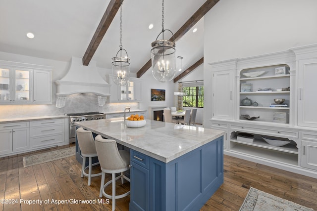 kitchen with white cabinets, beam ceiling, high end stove, and an island with sink