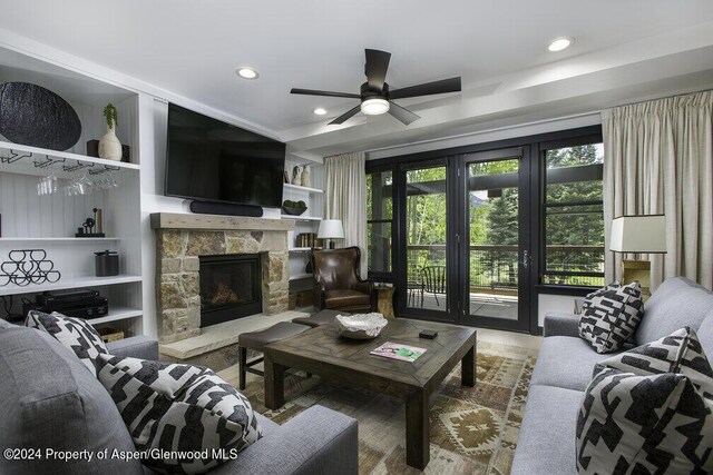 living room featuring ceiling fan, a stone fireplace, and built in shelves