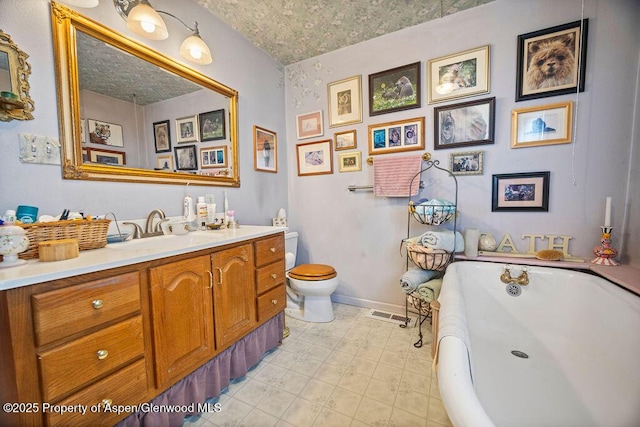 bathroom with a textured ceiling, toilet, vanity, baseboards, and a freestanding bath