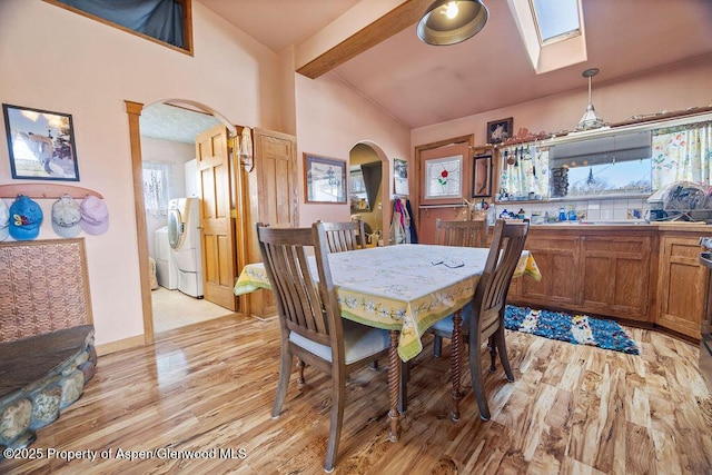 dining room with arched walkways, light wood finished floors, and vaulted ceiling with beams