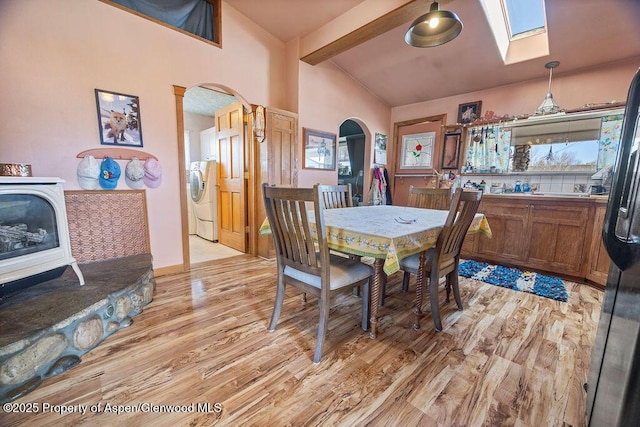 dining space with light wood-type flooring, vaulted ceiling with skylight, arched walkways, and washer / clothes dryer