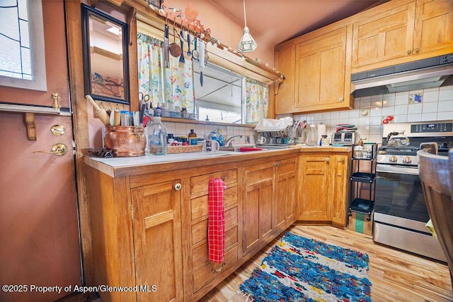 kitchen with under cabinet range hood, backsplash, light countertops, and stainless steel range with gas stovetop