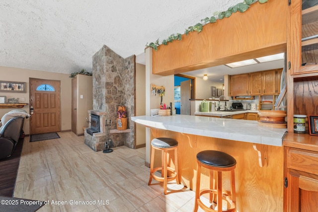 565 Sandrock Dr, Craig, CO 81625 - kitchen featuring a textured ceiling, brown cabinetry, a breakfast bar, tile countertops, and vaulted ceiling