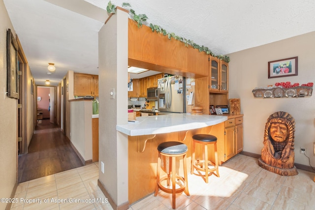 565 Sandrock Dr, Craig, CO 81625 - kitchen with stainless steel refrigerator with ice dispenser, light tile patterned floors, glass insert cabinets, a breakfast bar, and brown cabinetry