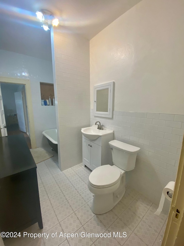 bathroom with vanity, tile patterned flooring, toilet, a tub to relax in, and tile walls