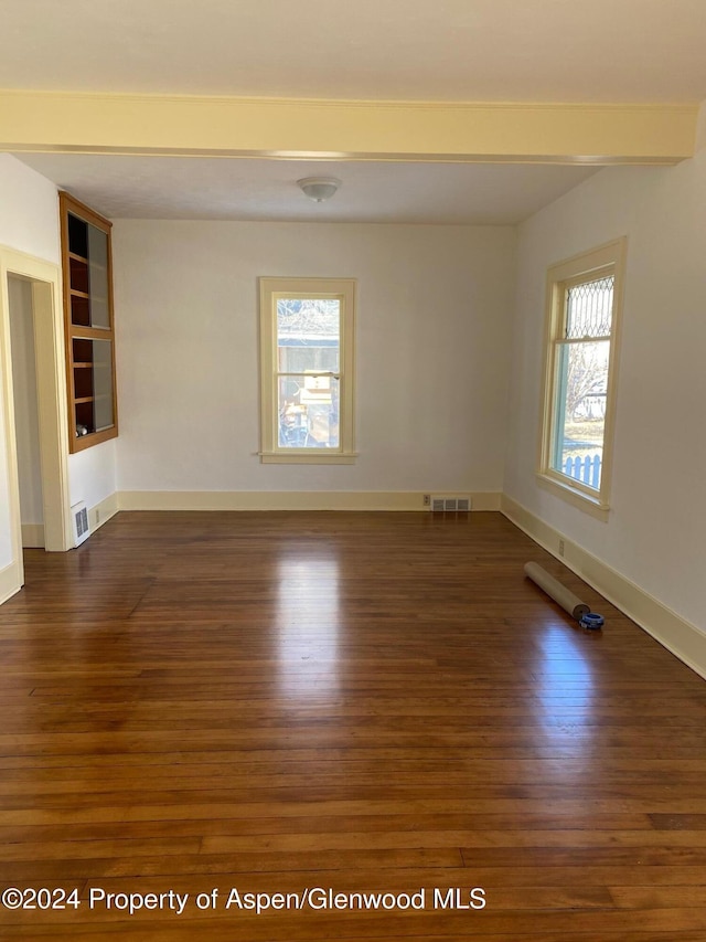 empty room featuring beam ceiling, built in shelves, and dark wood-type flooring