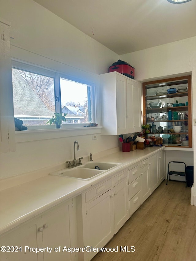 kitchen with light wood-type flooring, white cabinetry, and sink